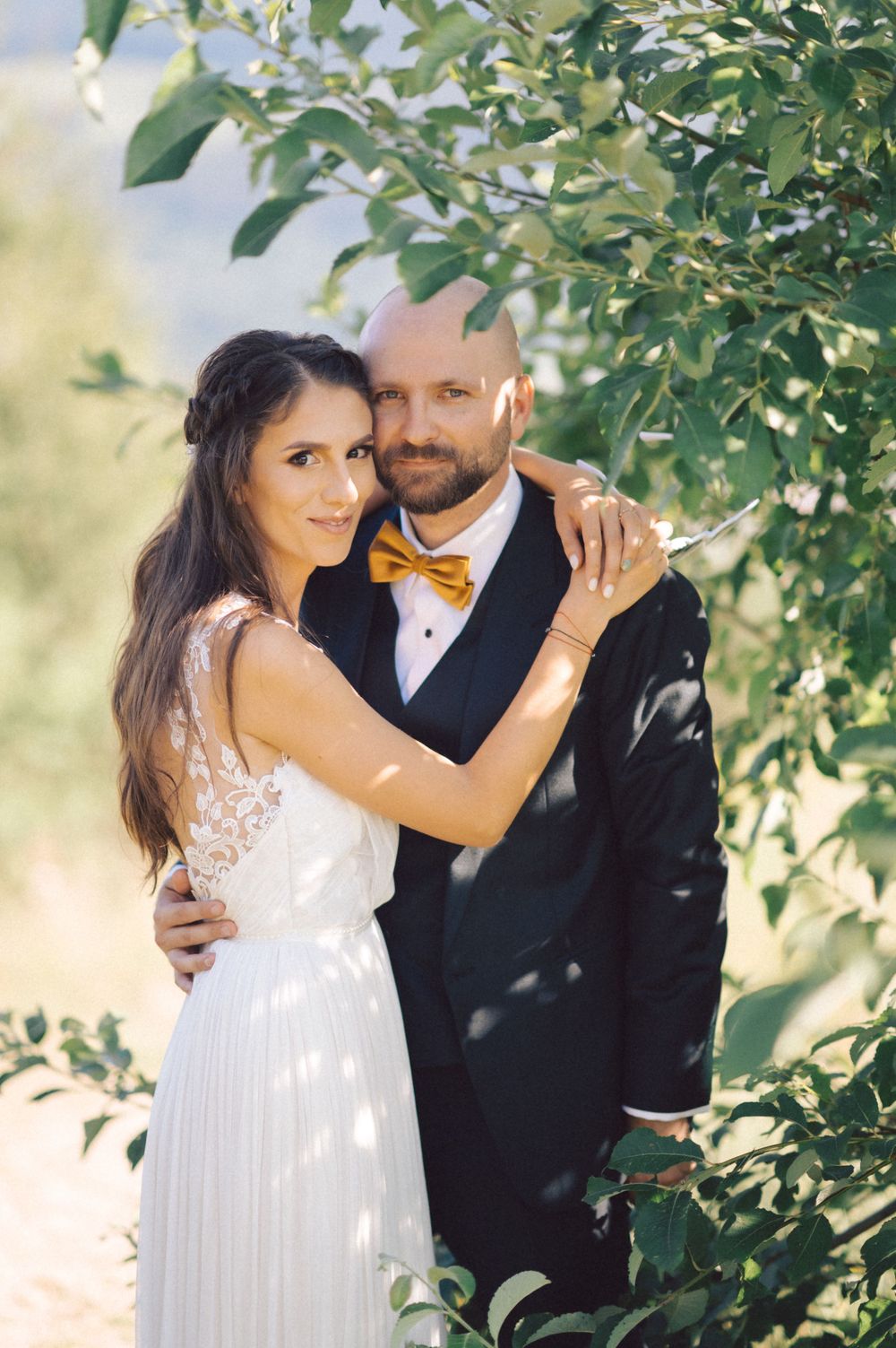 Romantic wedding portrait under green leaves with soft natural lighting.