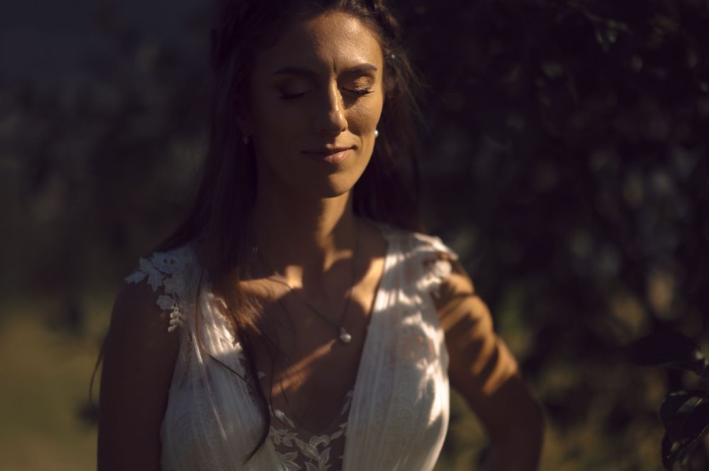 A romantic portrait of a bride in a white dress with dappled sunlight creating shadows on her face.