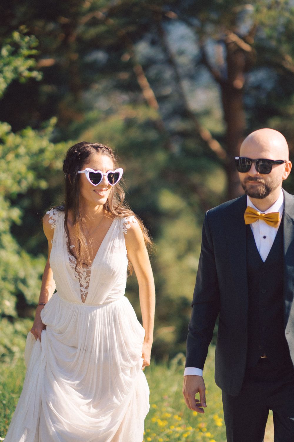 A stylish wedding couple in sunglasses posing together outdoors on a sunny day.
