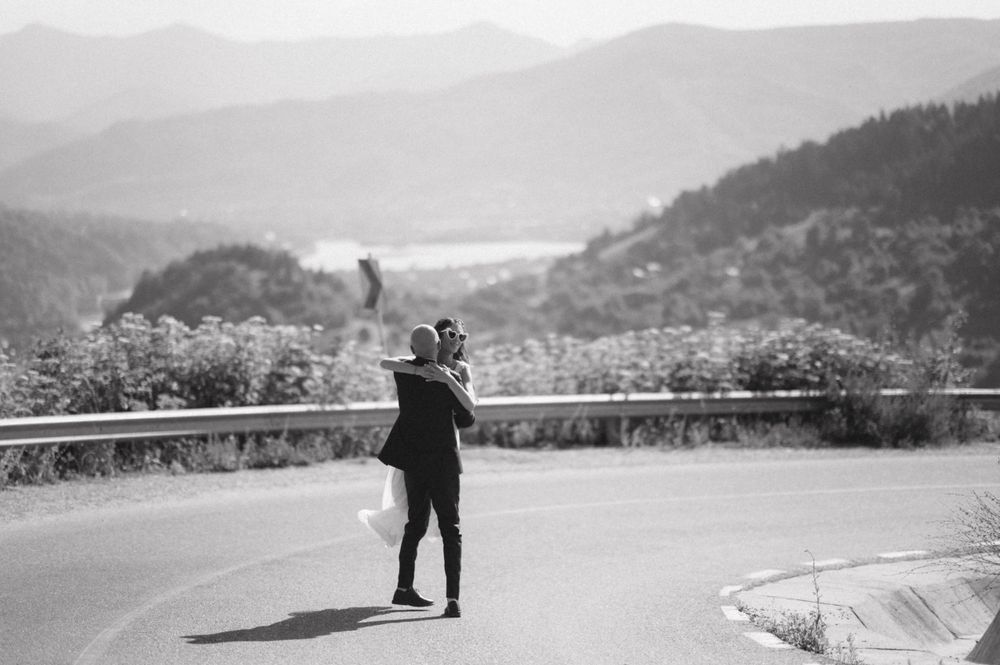 Black and white photo of a couple embracing on a mountain road with scenic valley views.