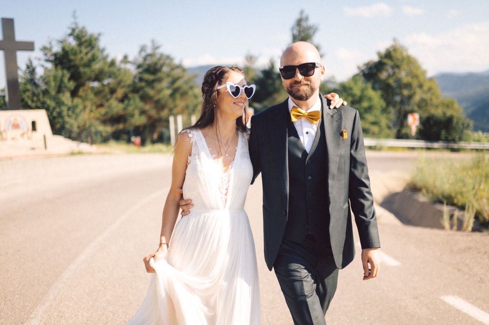 A wedding couple walking together on a sunny mountain road wearing stylish sunglasses.