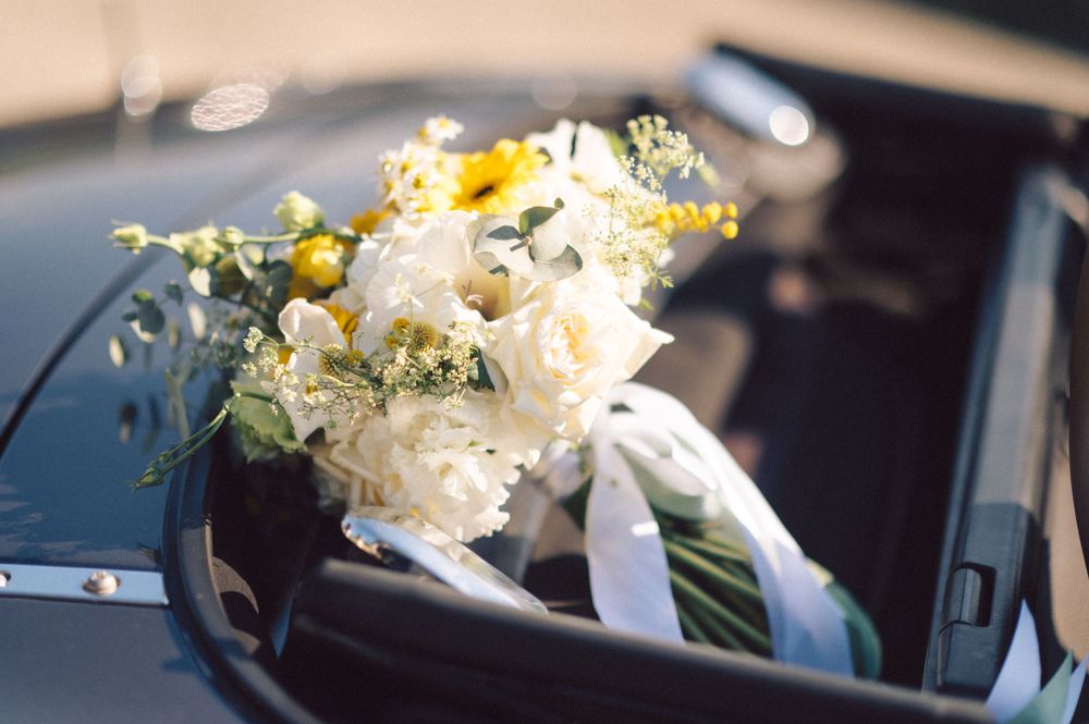 A beautiful white and yellow wedding bouquet resting in a black car.