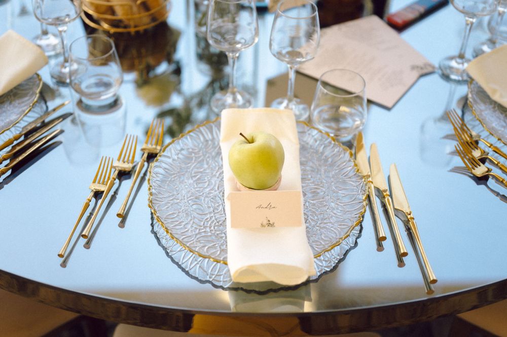 An elegant place setting with gold cutlery and a green apple on a glass charger plate.
