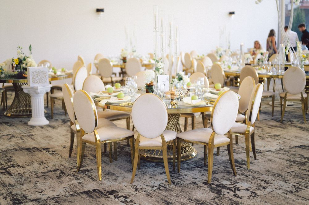 Elegant wedding reception table setup with cream chairs and gold accents in an outdoor setting.