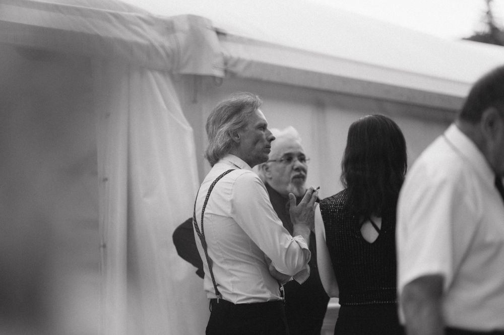 Black and white candid shot of guests conversing at a formal event under a tent.