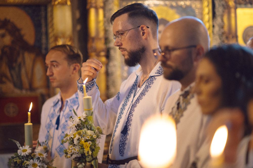 People in embroidered ceremonial attire stand by candlelight.