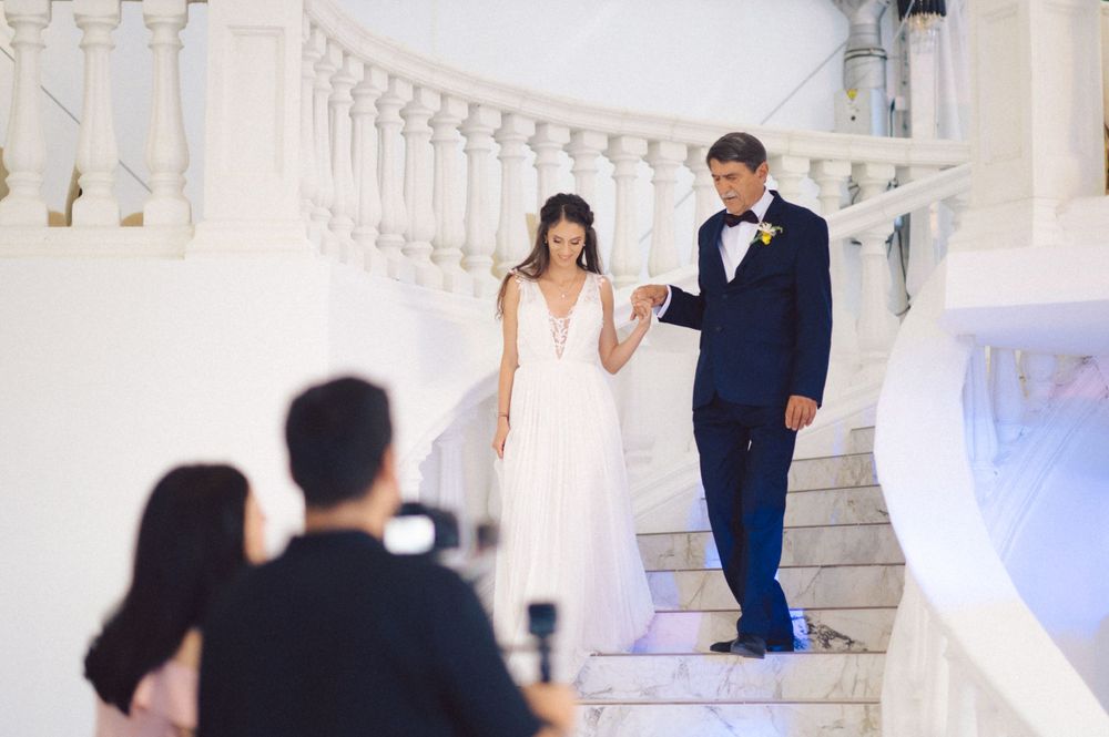 Couple on grand white marble staircase being photographed during their wedding celebration.