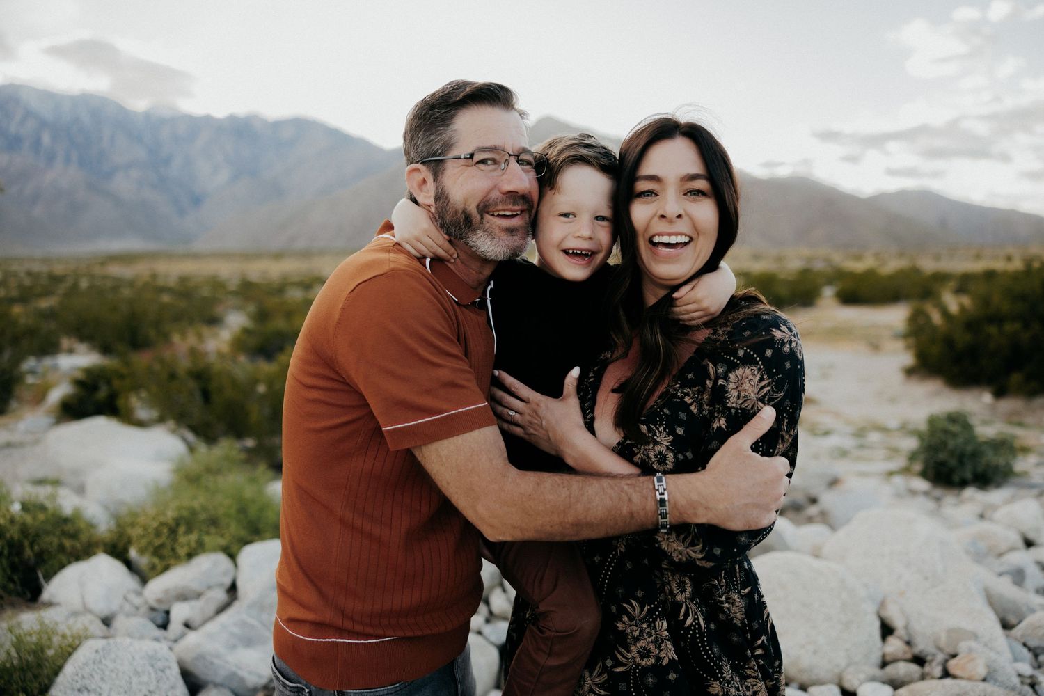 A loving family embraces while posing for a portrait in front of majestic mountains and desert landscape.
