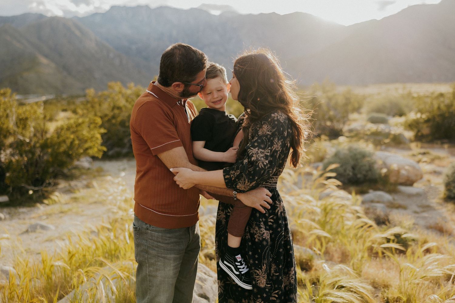 Family shares intimate moment together in desert setting with mountains in background.