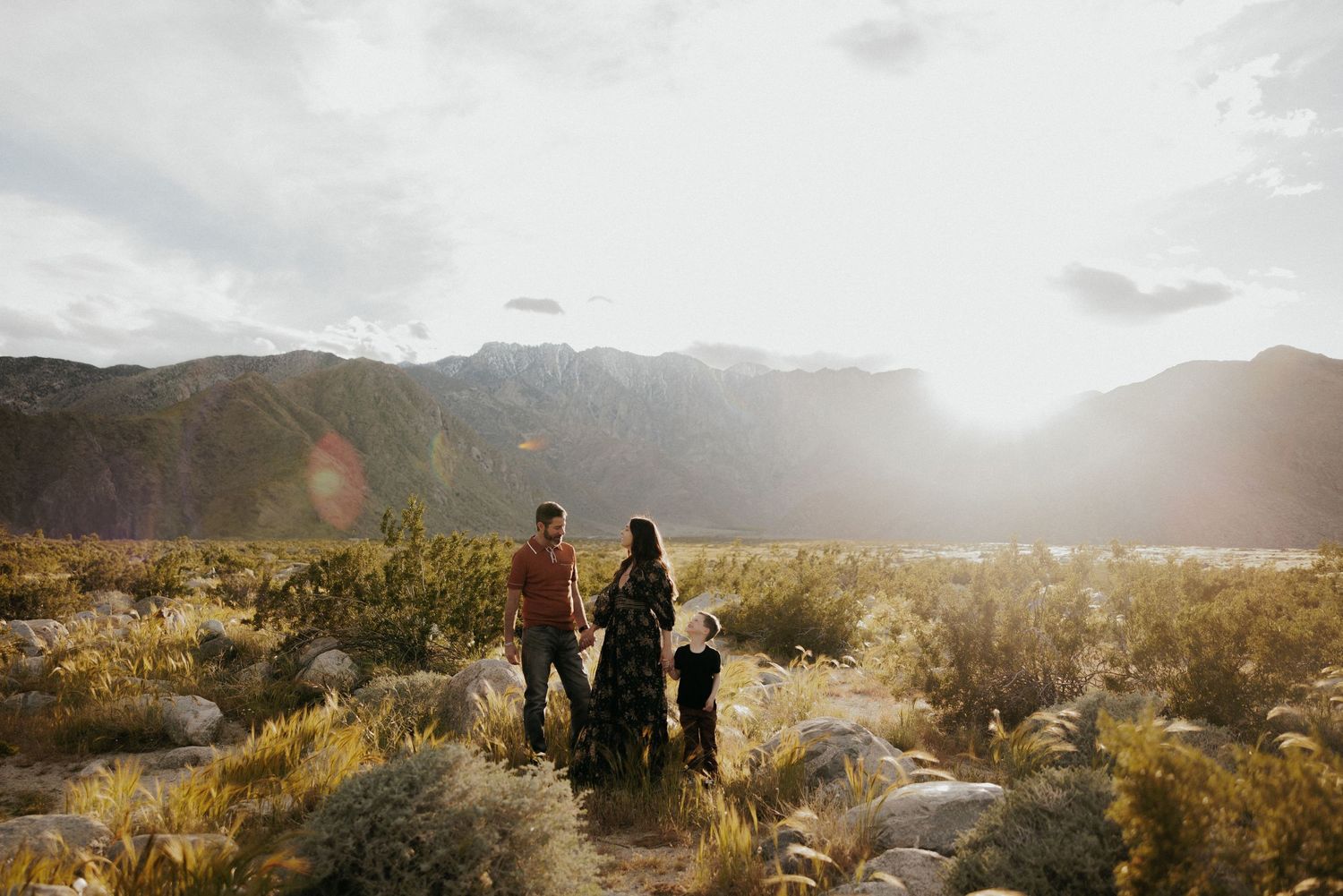 Group walking along a desert trail with mountains and sunlit shrubs in the background.