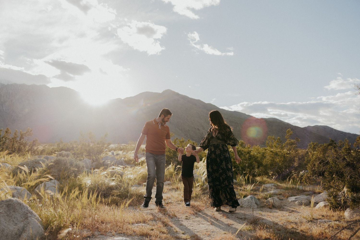 Couple walking hand in hand on desert trail during golden hour with mountains in background.