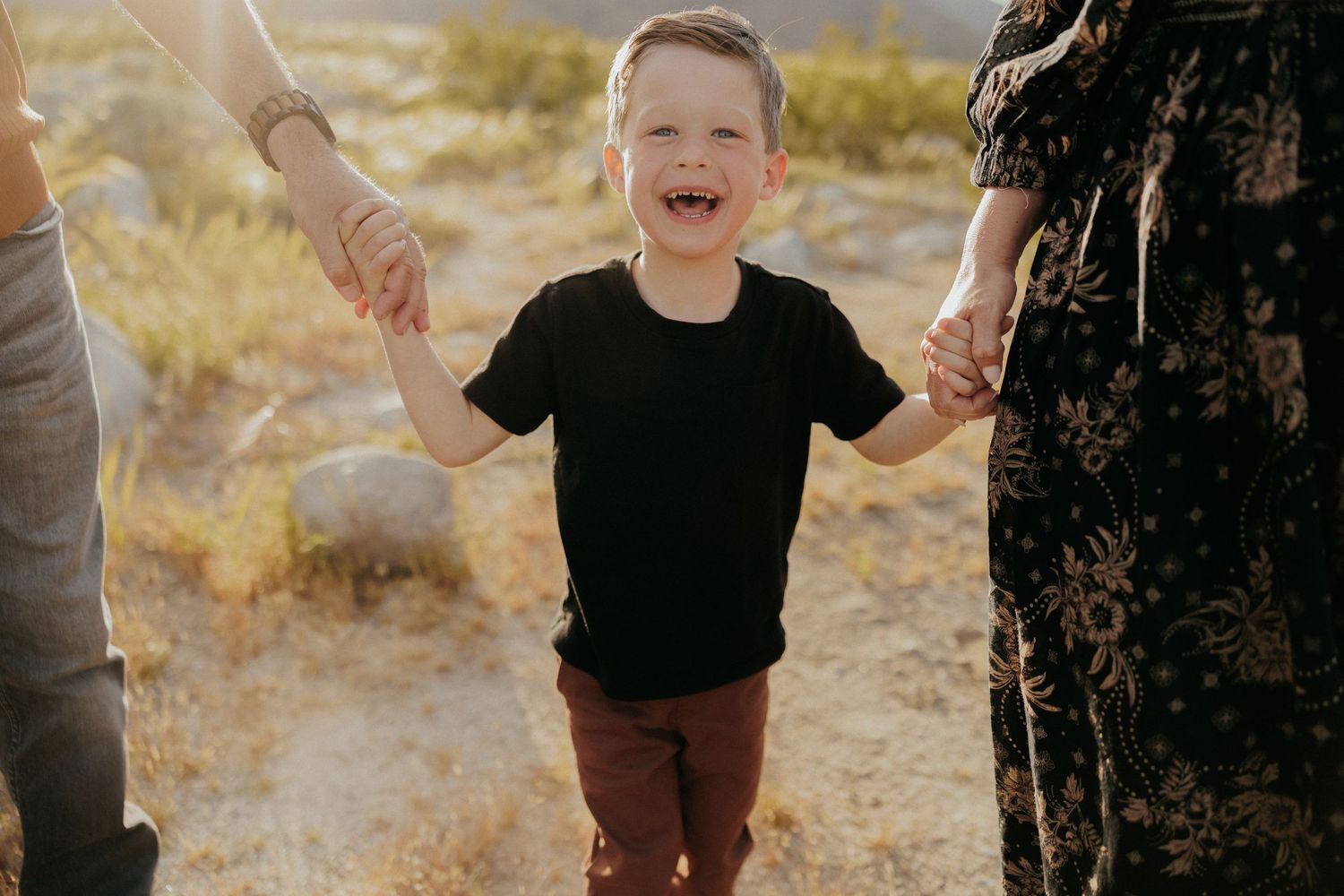 Joyful child laughing while holding hands with parents on desert path.