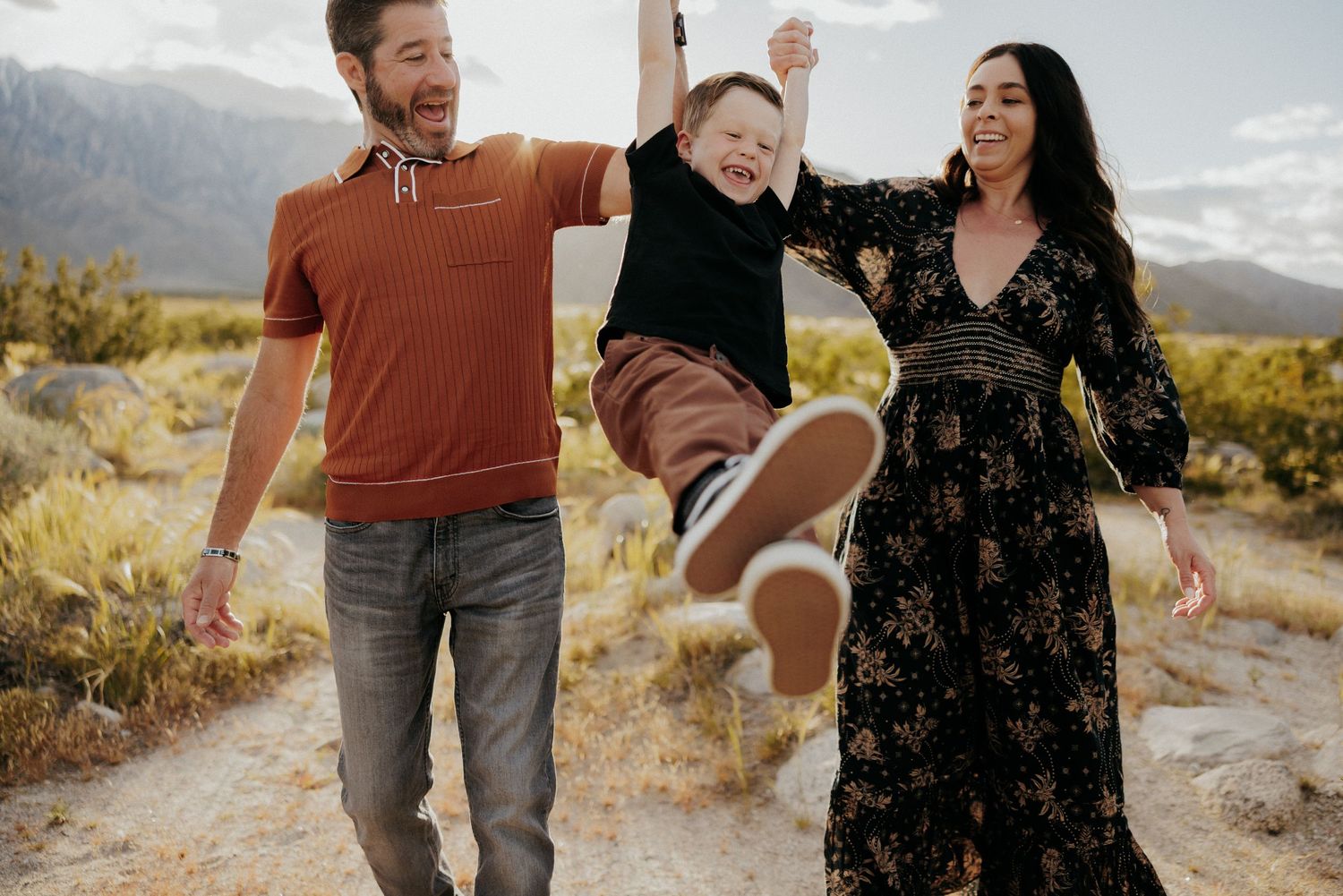 Family playing and jumping together on desert trail during sunset photoshoot.