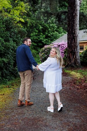 Couple holding hands on a wooded path with blooming azaleas and greenery in the background.