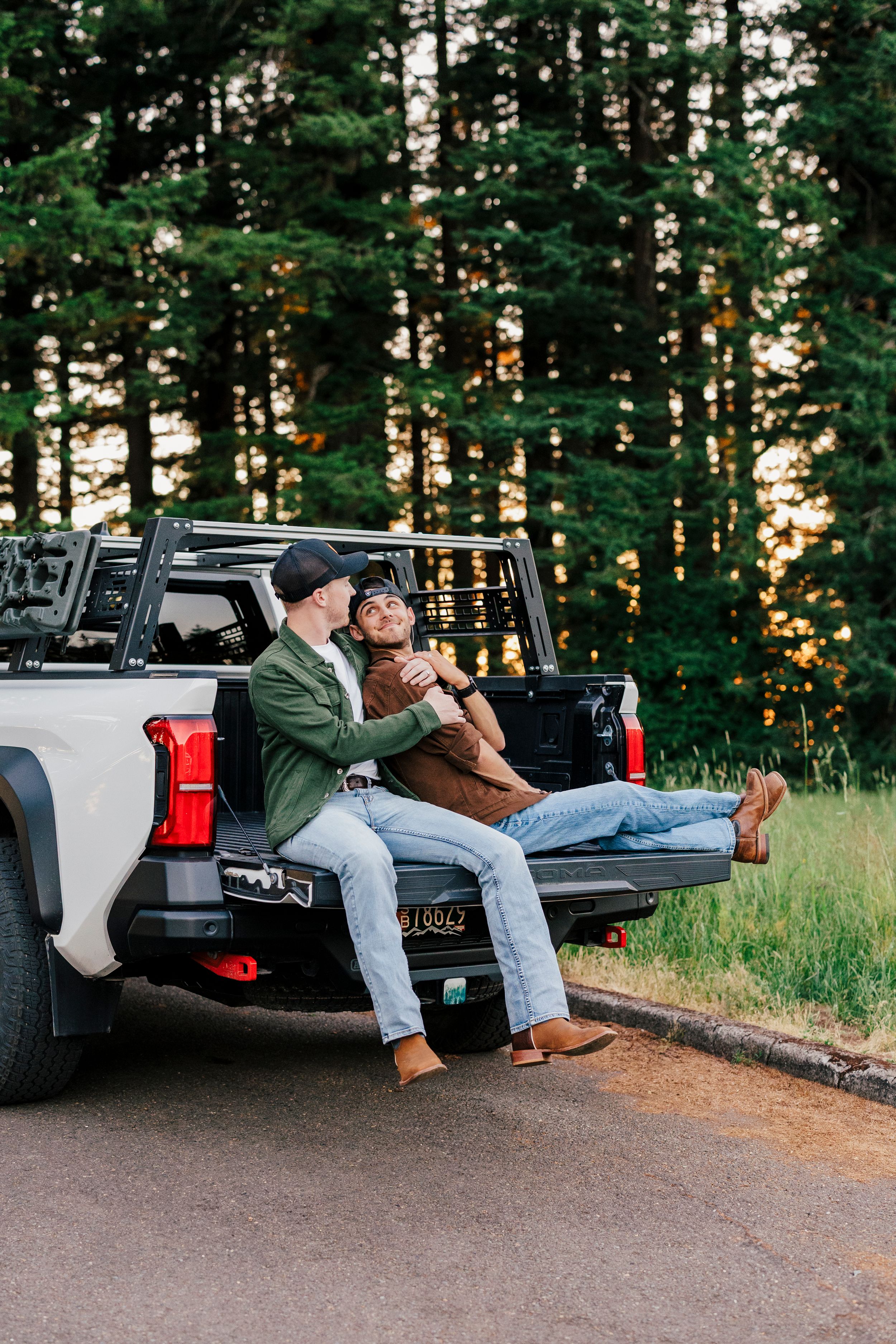 Two people relaxing in back of pickup truck at sunset in forest, enjoying casual outdoor moment together.