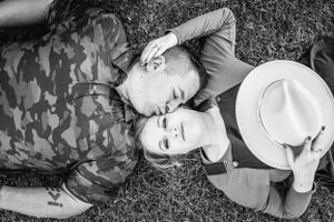 A black and white photo of a couple lying on grass while holding a hat.