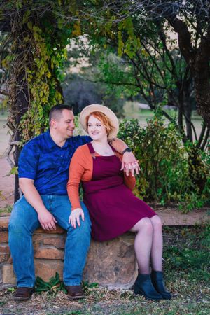 Couple sitting on stone wall under ivy-covered arch in garden setting.