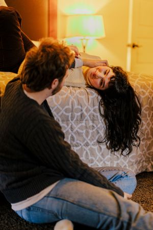 A loving couple shares a playful moment on a patterned couch in warm ambient lighting.