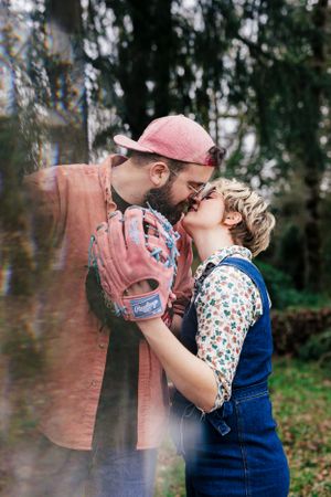 A couple wearing floral print and denim overalls share a romantic moment in a dreamy outdoor setting.
