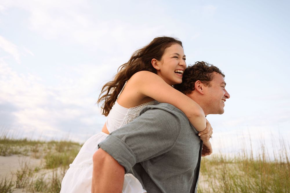 Playful piggyback ride along coastal dunes during sunset.