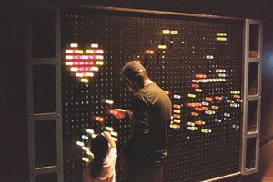 Colorful light display on a dark pegboard creates a heart shape and other patterns.