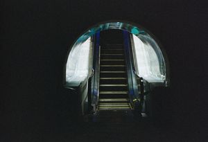 Futuristic curved escalator entrance with illuminated white walls.