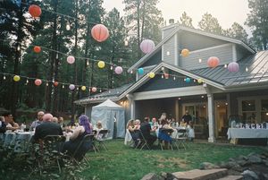 Colorful paper lanterns hang across an outdoor evening venue with pine trees.