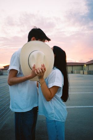 Couple in white shirts sharing intimate moments behind a cowboy hat at sunset.