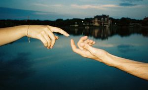 Hands reaching across water surface reflecting blue sky and clouds.