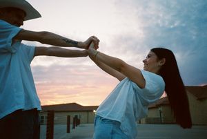Dancing couple in white shirts silhouetted against sunset sky.