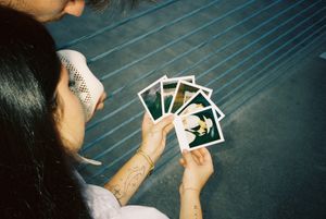 Hands holding and looking through polaroid photographs on dark surface.