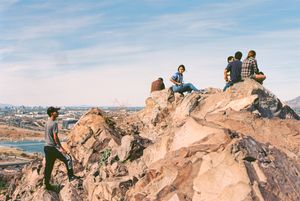Group of people sitting on rocky outcrop overlooking desert landscape.