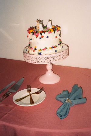 White decorated wedding cake on a pink stand with blue napkins and place settings.