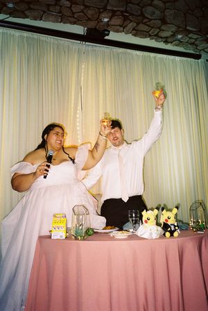 Wedding party in white attire celebrating enthusiastically at a head table.