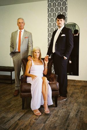 Wedding party posing together in formal attire on hardwood floors against a patterned wall.