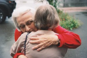 People sharing warm embraces outdoors on a sunny day.
