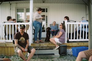 People relaxing on a porch with white railing during a casual gathering.