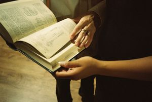Hands gently turn pages of an open book against a dark background.