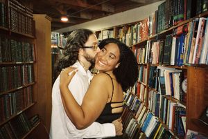 A romantic moment unfolds between two people in a library with filled bookshelves.
