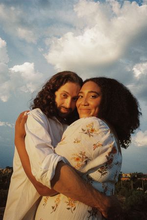 A tender embrace captured outdoors with dramatic clouds in the background.