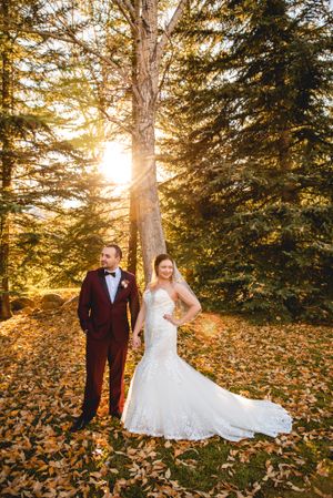 Wedding couple poses in autumn forest with golden sunlight streaming through trees.