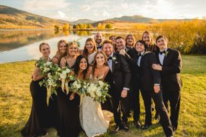 Wedding party group photo by lake with autumn mountains in background.