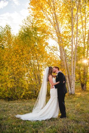 A romantic autumn wedding photo with golden aspen trees and sunlight filtering through the branches.