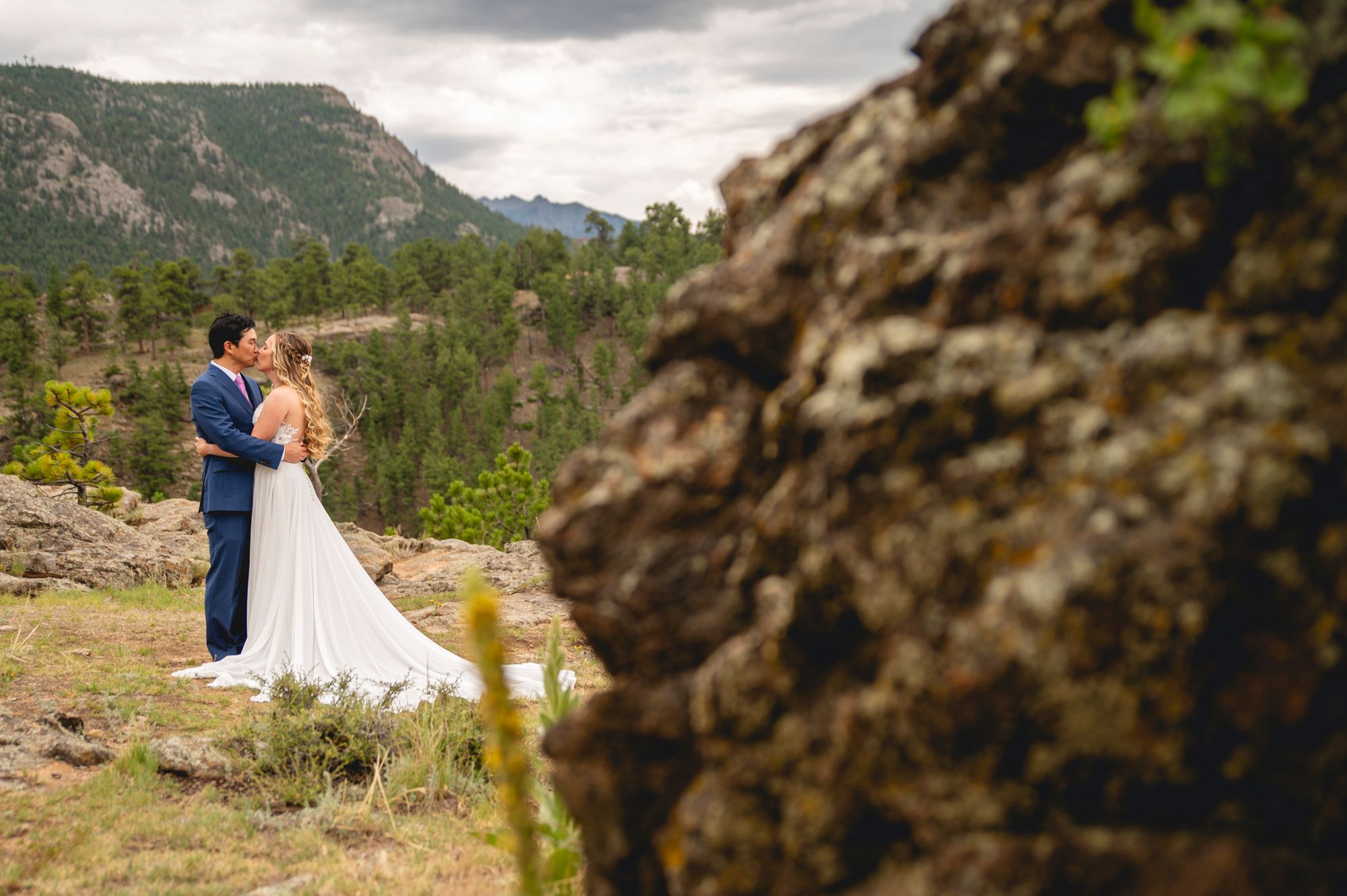 Wedding couple shares intimate moment on mountain overlook with dramatic rocky landscape.