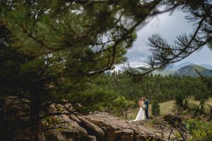 Distant wedding photo framed through pine branches with mountains in background.