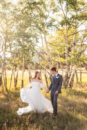 A newlywed couple holds hands in a sun-dappled aspen grove during their romantic golden hour photo session.
