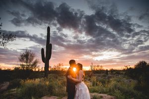 Silhouetted wedding couple kisses at sunset with saguaro cactus in desert landscape.