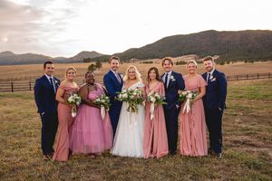 Wedding party poses in formal attire against mountain backdrop at sunset.