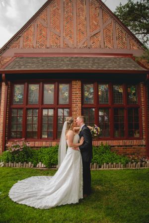 A couple shares an intimate moment outside a brick building with ornate Victorian architectural details and large windows at Wellshire Inn