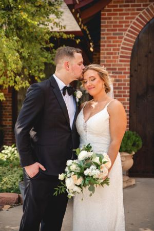Intimate wedding portrait in front of brick archway with white floral bouquet.